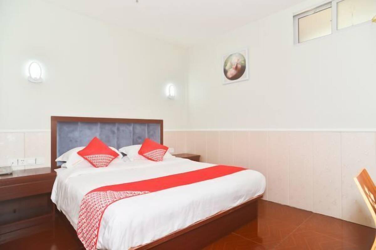 Une chambre d’hôtel avec un lit, des tables de chevet, une commode, un tableau accroché au mur et une fenêtre.