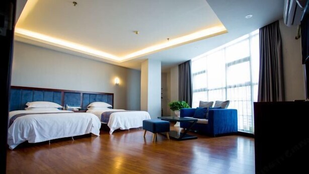 Une chambre d’hôtel avec deux lits, un canapé, une petite table et une grande fenêtre.