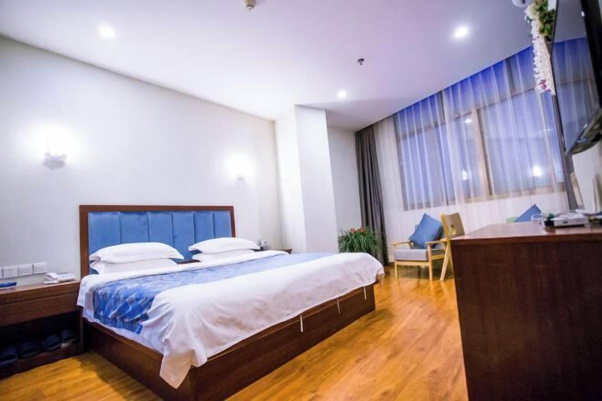 Une chambre d’hôtel avec un grand lit, une table de chevet en bois, un bureau et une fenêtre avec des rideaux.