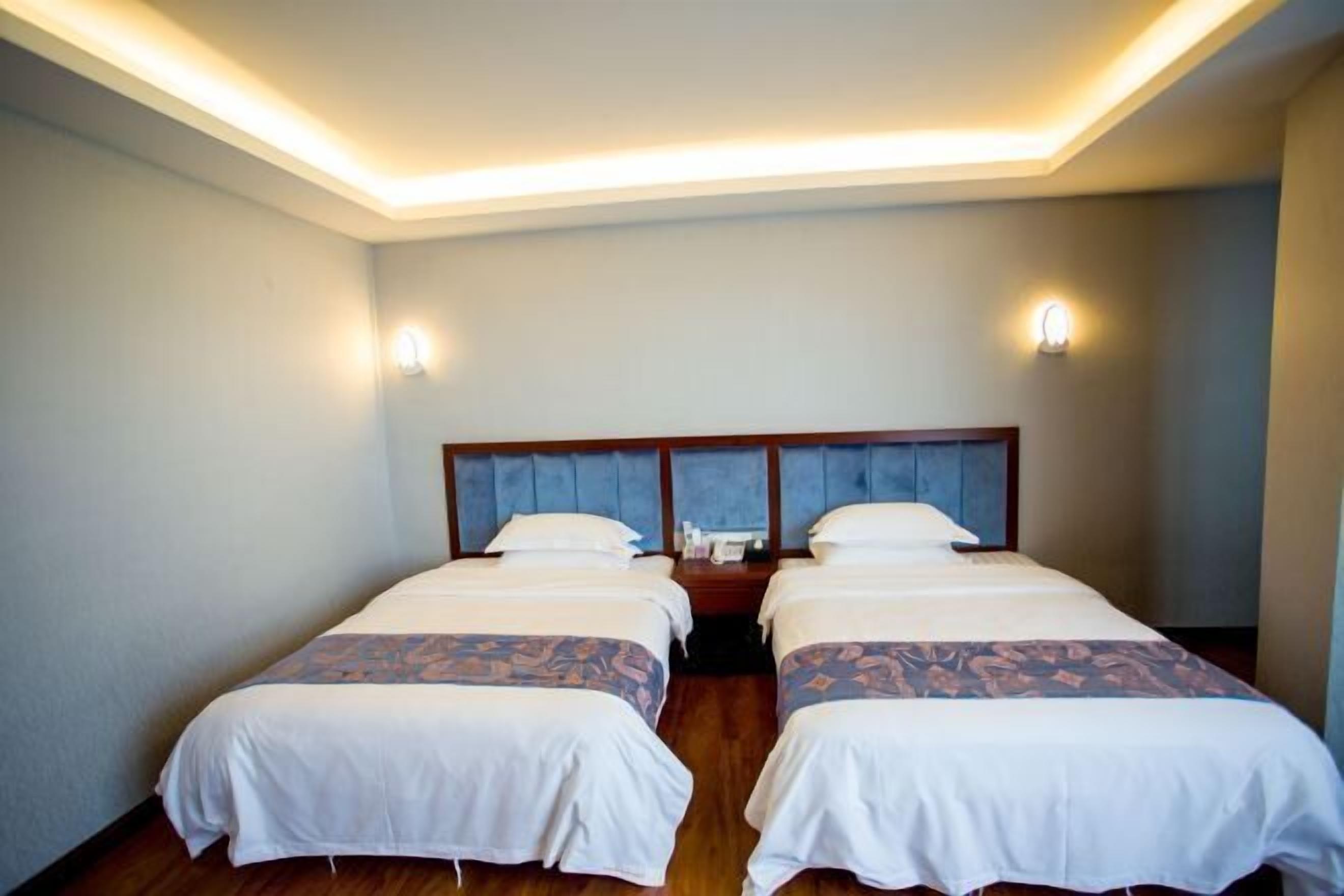 A hotel room with two beds, a wooden headboard, and wall-mounted lights.