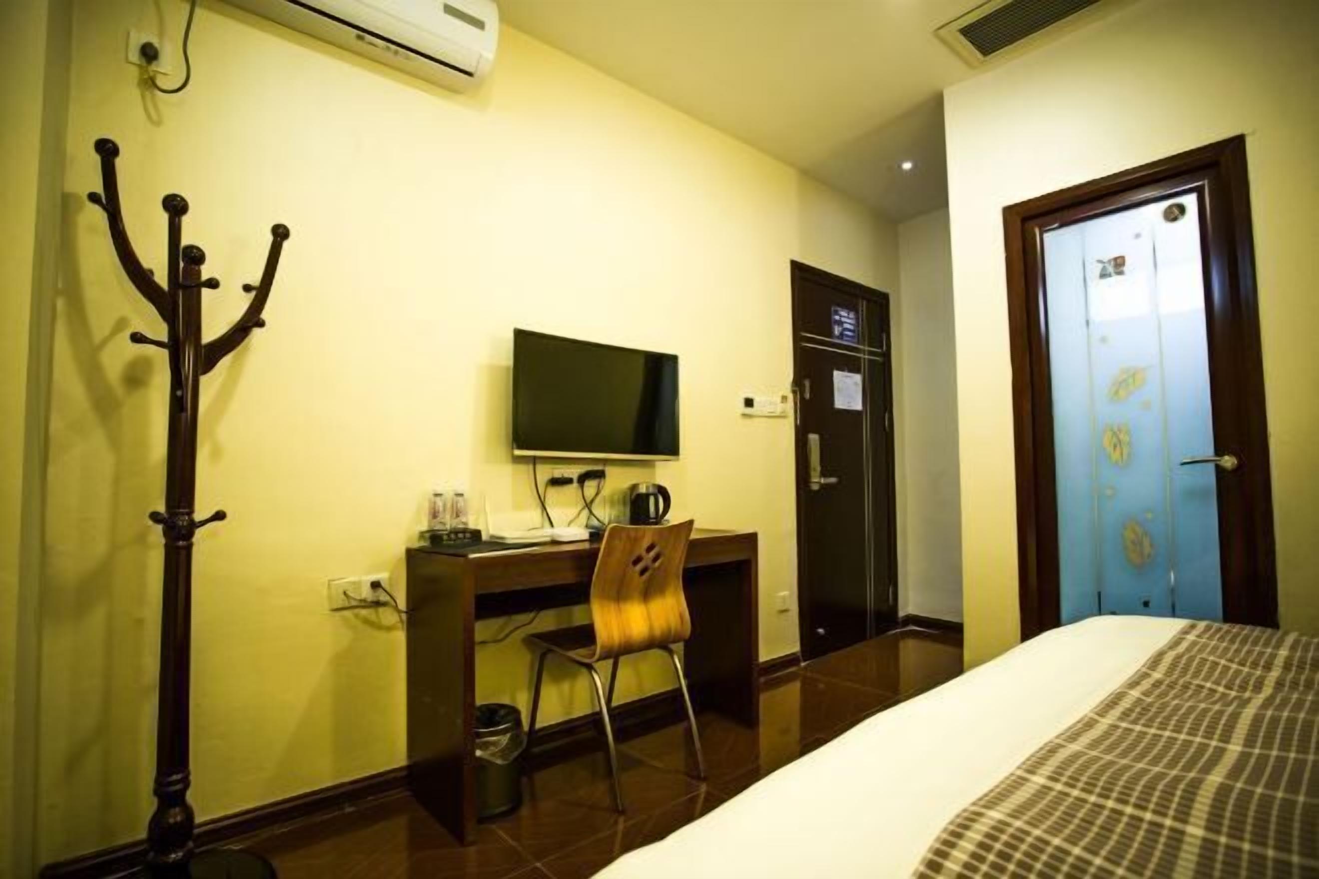 Ein Hotelzimmer mit einem Bett, einem Schreibtisch mit Stuhl, einem Fernseher und einem Kleiderständer.