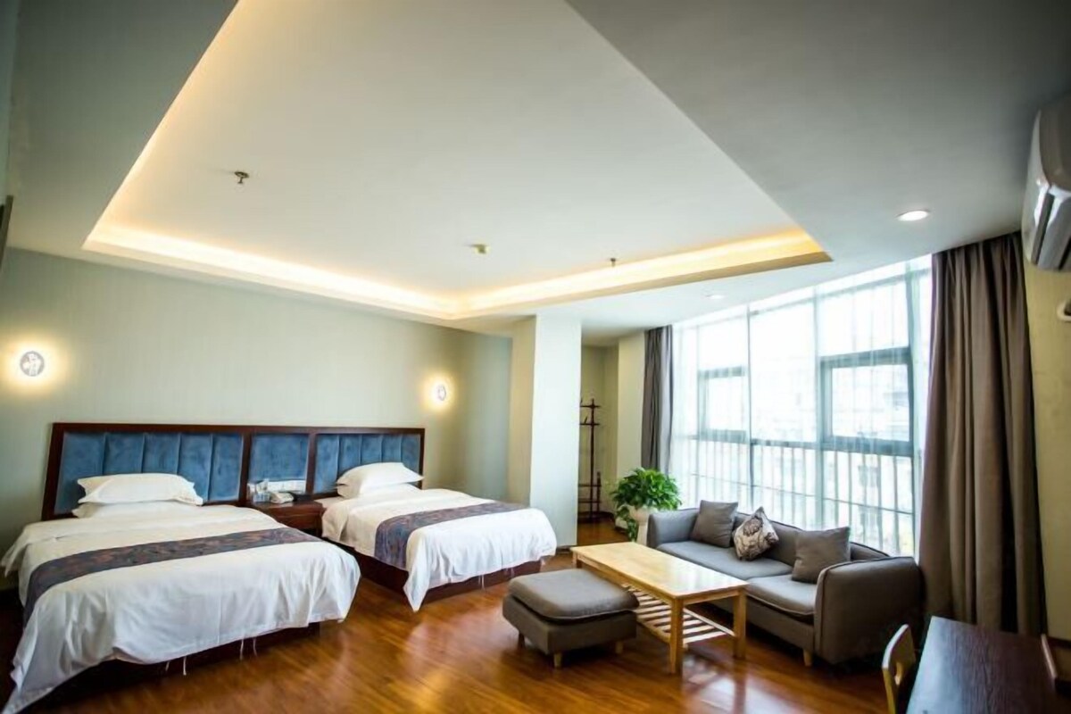 Quarto de hotel com duas camas, um sofá, uma mesa de centro e janelas amplas.