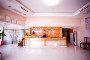 A hotel reception area with a receptionist, a reception desk, a large potted plant, and a modern chandelier. - Dongnanhong Business Hotel (Xianyou)