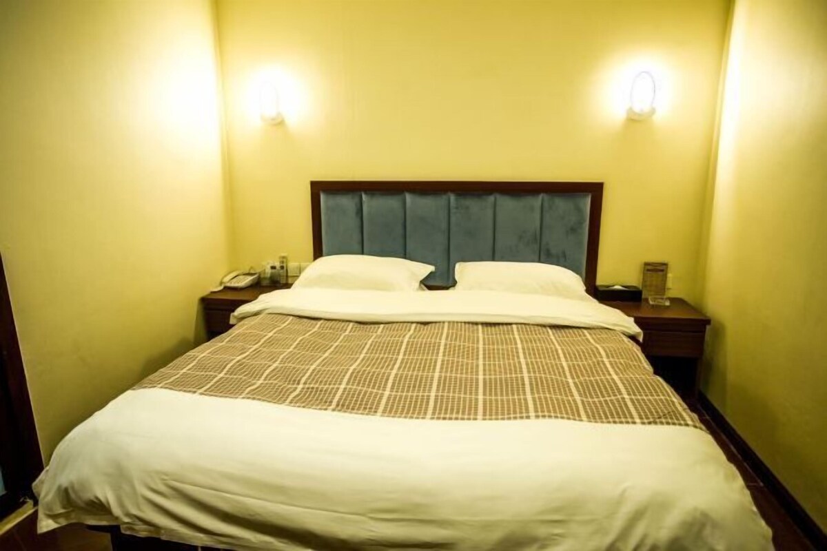 Quarto de hotel com uma cama grande, duas mesas de cabeceira e uma mesinha de canto com abajur.