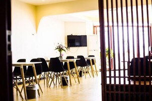 Un salón de conferencias con una larga mesa, sillas, un televisor y una planta.