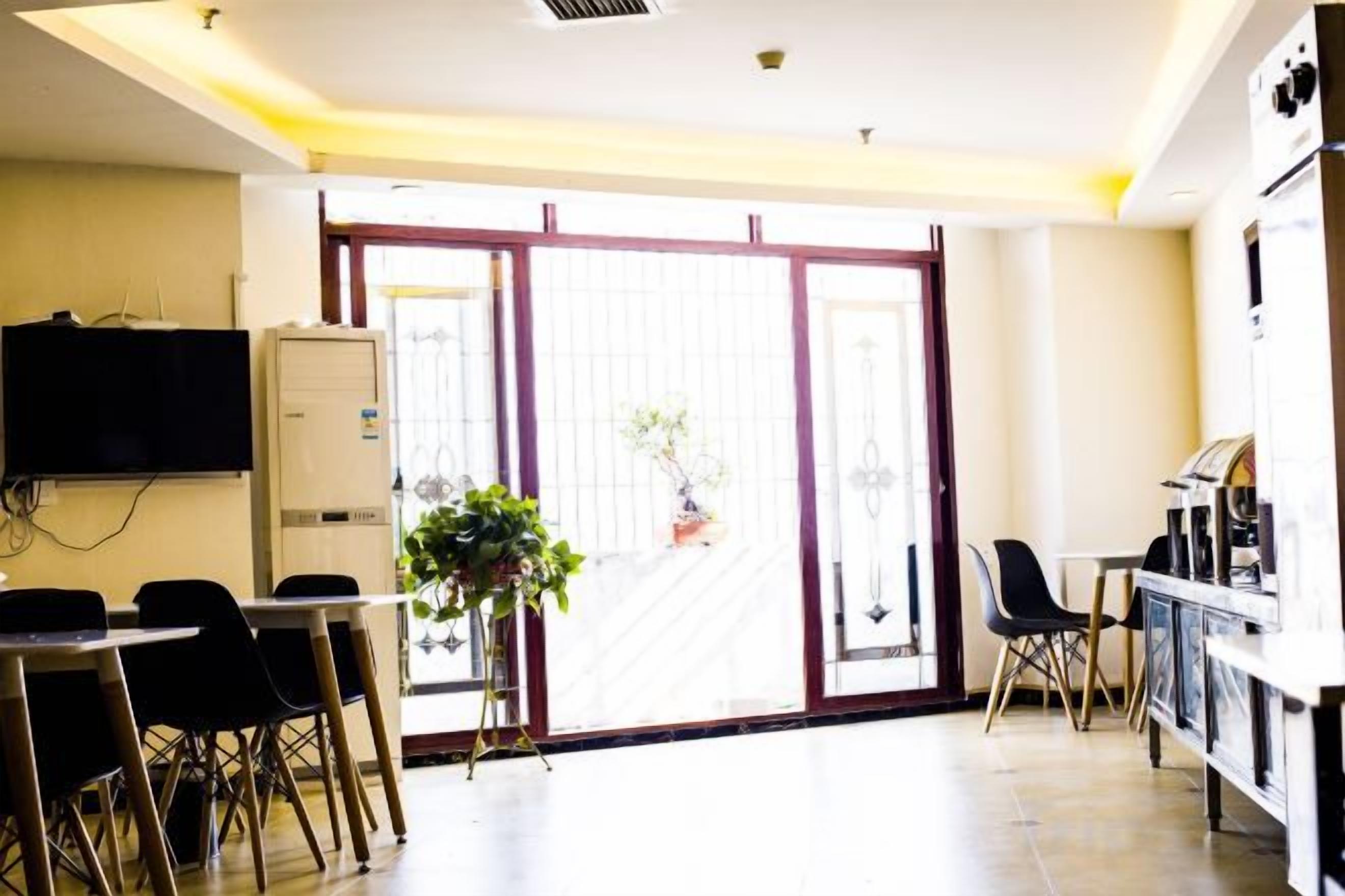 A room with a sliding glass door, a television mounted on the wall, a table with chairs, and a refrigerator.
