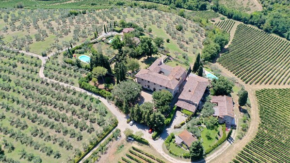 Vista aérea de una extensa propiedad con un edificio central rodeado de viñedos y jardines.