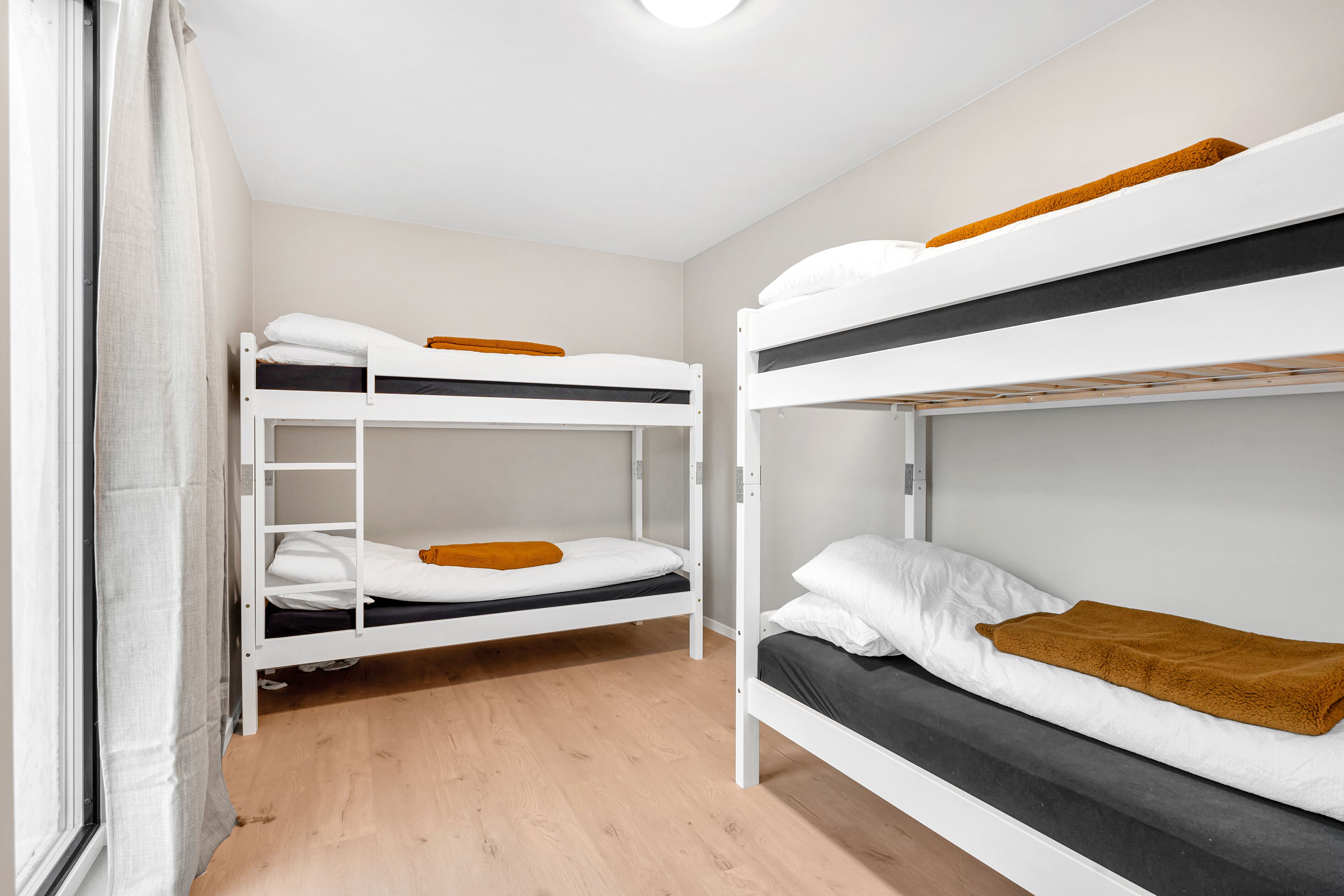 A bunk bed room with a window, wooden flooring, and white walls.
