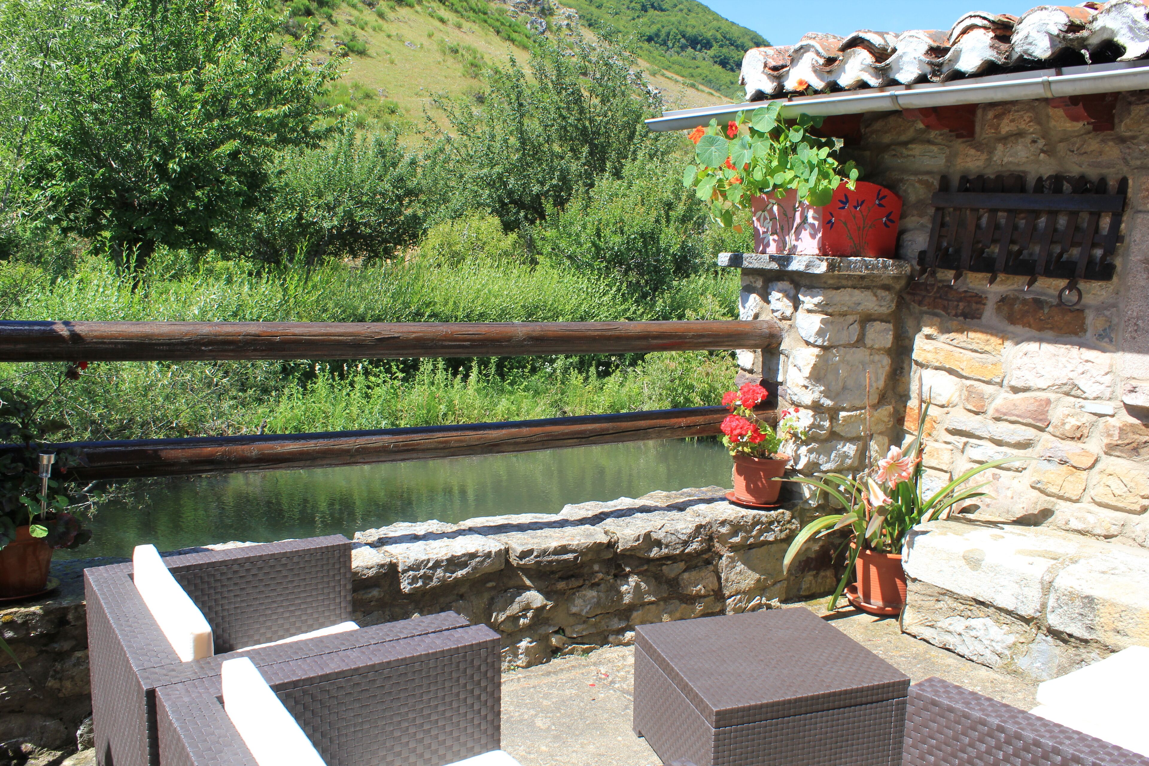 A stone building with a rustic balcony overlooking a body of water, surrounded by greenery.