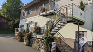 Un edificio a due piani con una scala, piante da esterno e una cassetta postale.