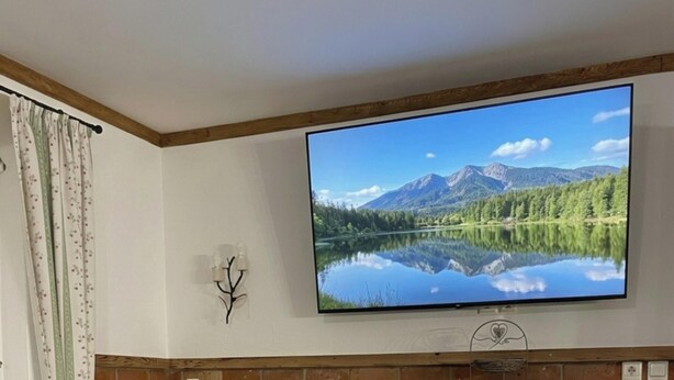 Un televisore a schermo piatto montato a parete mostra una veduta di un lago di montagna.