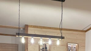 Zona pranzo con tavolo in legno, quattro sedie, lampadario e un vaso con fiori.