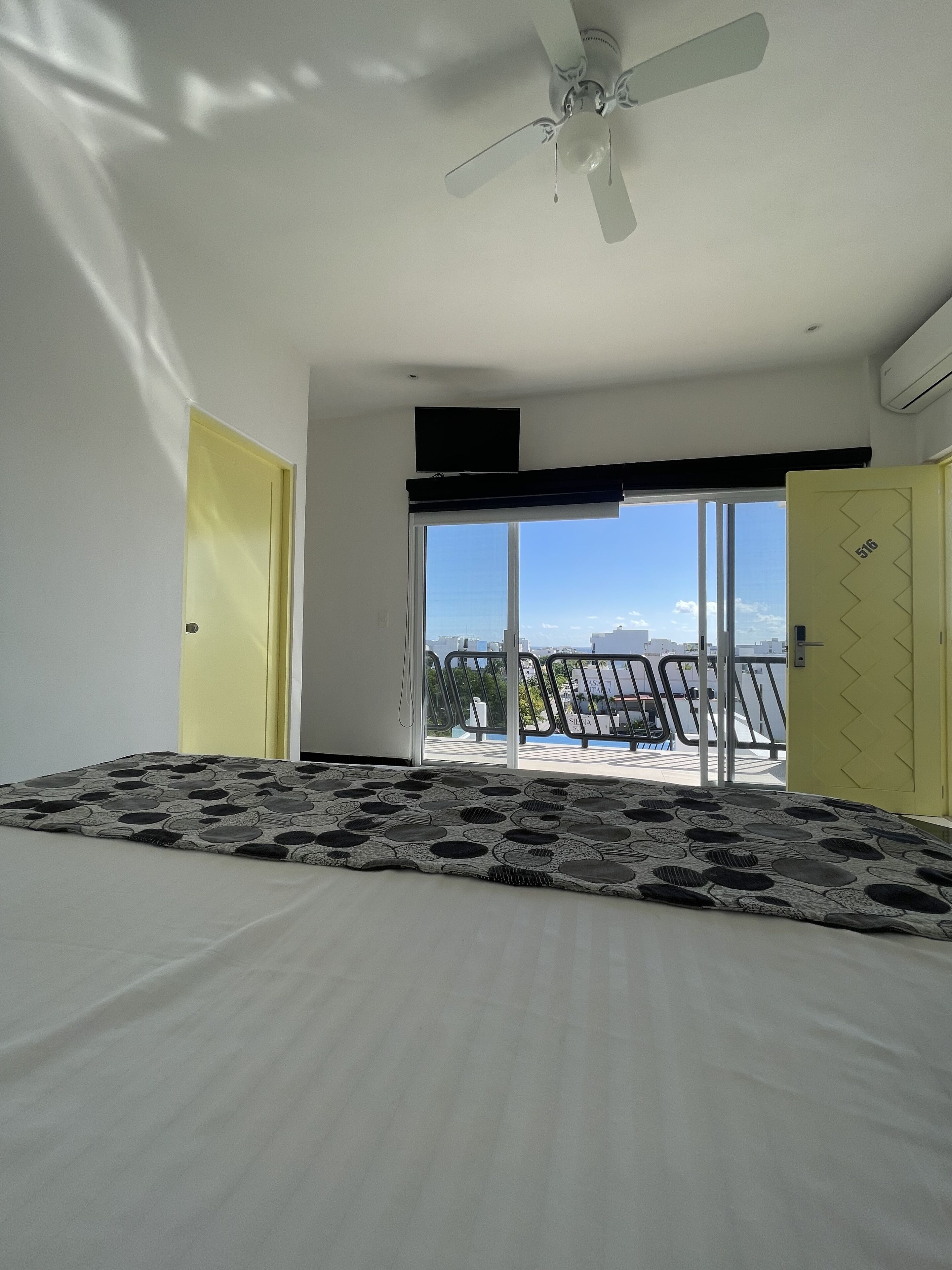 Una camera da letto con un letto, una ventola a soffitto, un'ampia finestra e vista sulla città.