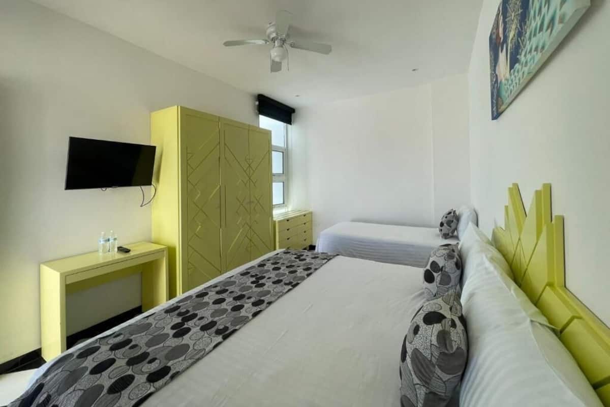 Un dormitorio con cama, escritorio, televisor y ventilador de techo.