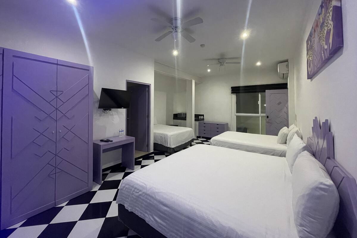 Una habitación de hotel moderna con dos camas, un televisor de pantalla plana, un ventilador de techo y piso a cuadros.