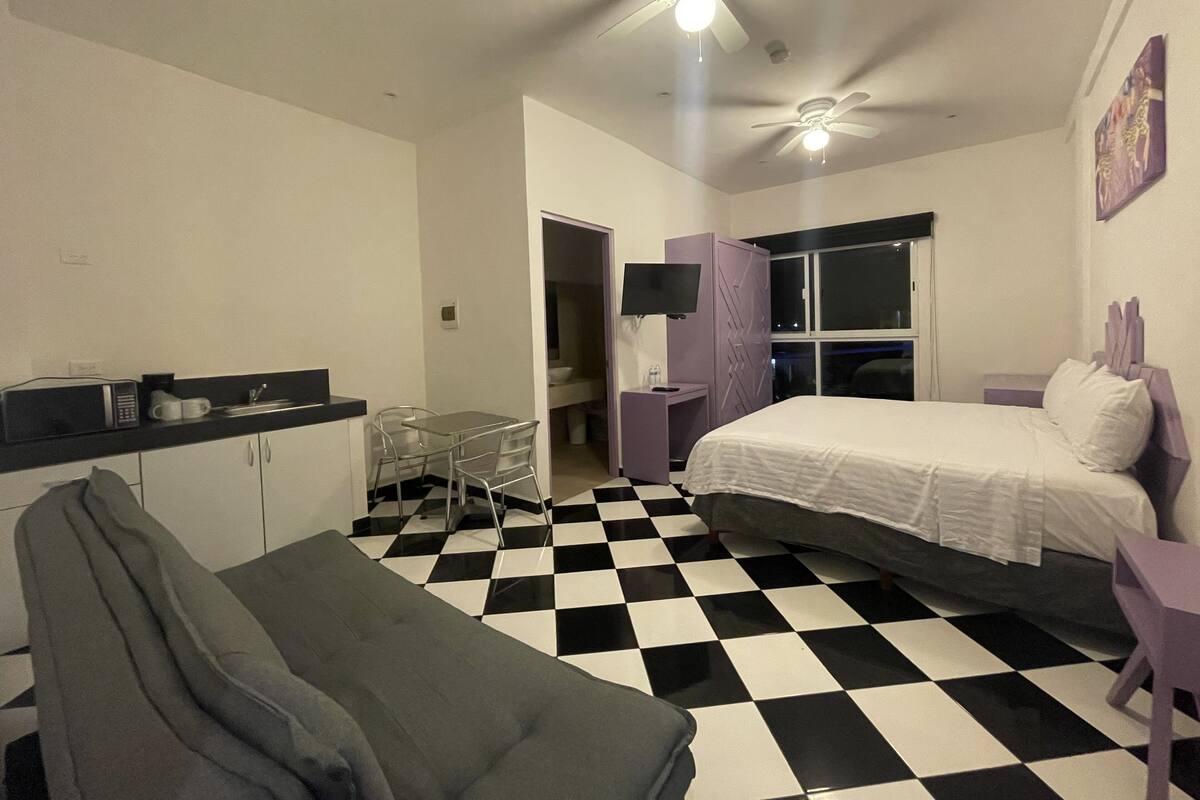 Habitación de hotel con suelo a cuadros, una cama, un escritorio con silla, un televisor y una ventana.