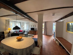 Un salon chaleureux avec une table ronde, un canapé et un téléviseur. Il y a une fenêtre avec des rideaux et une cheminée.