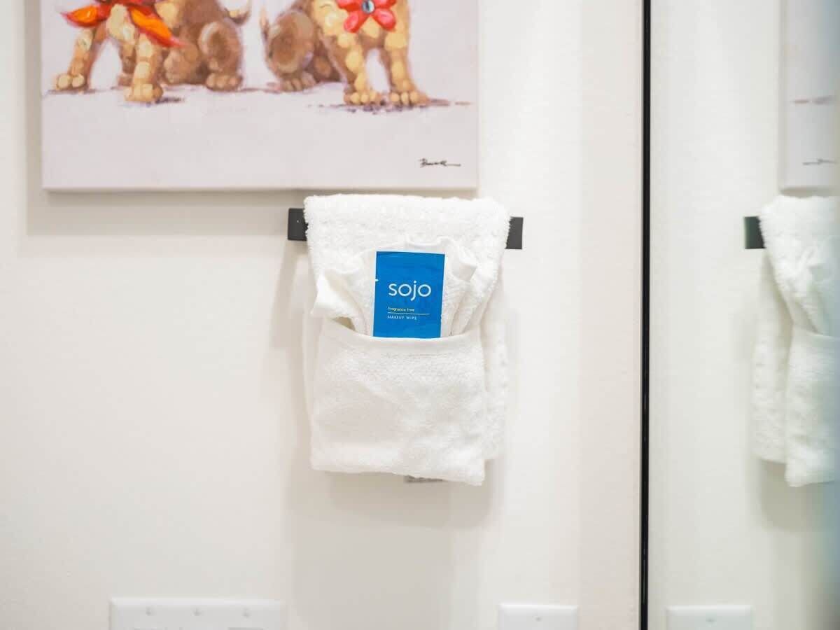 A white towel hanging on a black hanger with a blue label that reads "sojo".