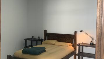 Een slaapkamer met een houten bed, een nachtkastje, een bureau en een lamp.