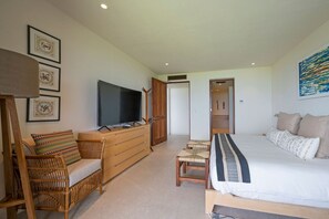 Ein modernes Hotelzimmer mit einem großen Bett, einem Fernseher, einer Holzkommode und einer Sitzecke mit einem Sessel und einem kleinen Tisch.