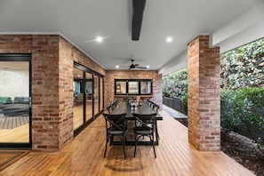 A spacious patio with a wooden deck, a long dining table with chairs, and brick walls.