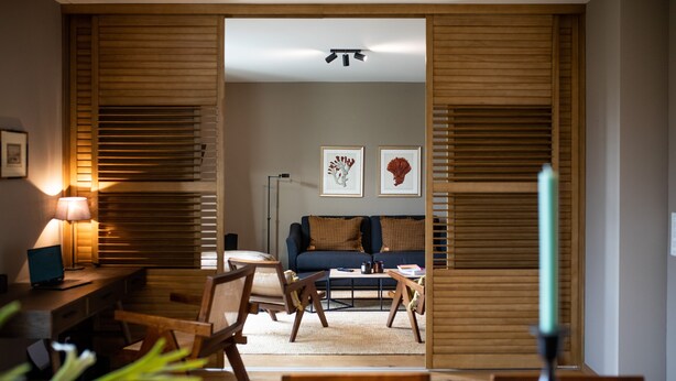 Uma sala de estar moderna com sofá, mesa de centro e cadeiras. Há uma luminária sobre uma escrivaninha e obras de arte emolduradas na parede.