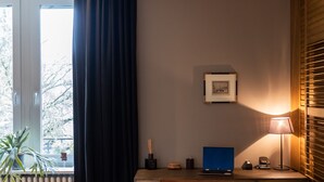 Quarto com escrivaninha de madeira, laptop, cadeira, luminária e janela com cortina.