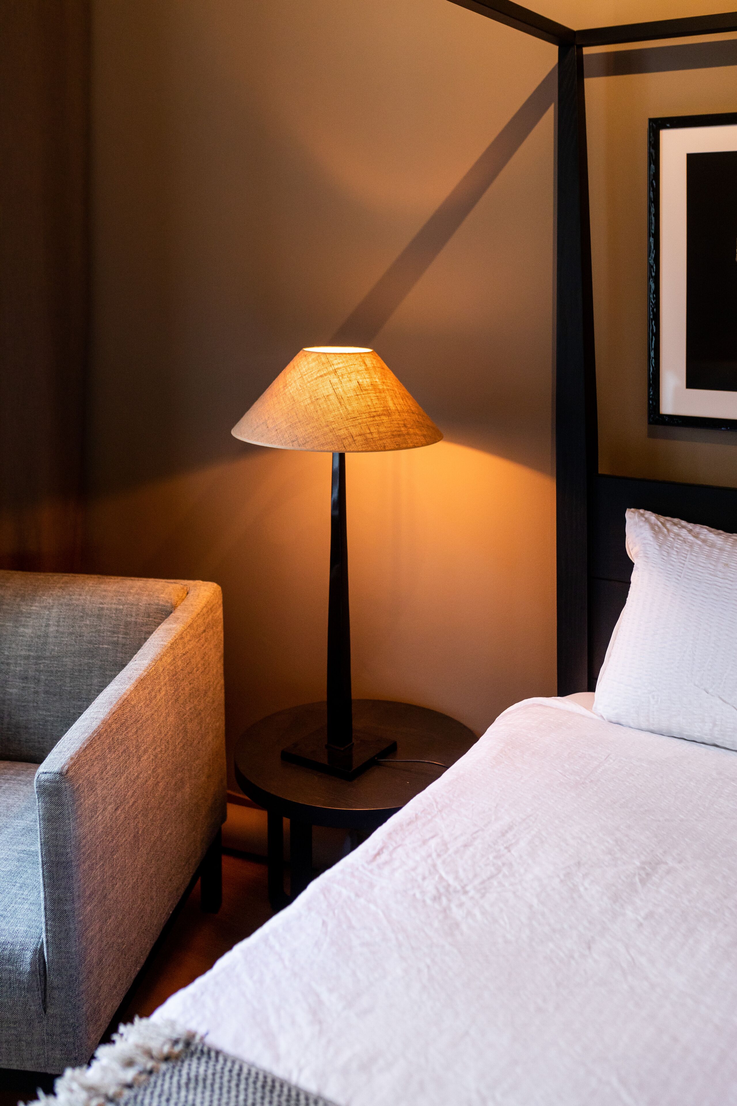 Une chambre d’hôtel avec un lit, une chaise, une table ronde et une lampe.