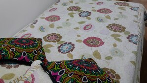 Ein Schlafzimmer mit einem blumengedeckten Bett, einer Holztür und einer weißen Wand.