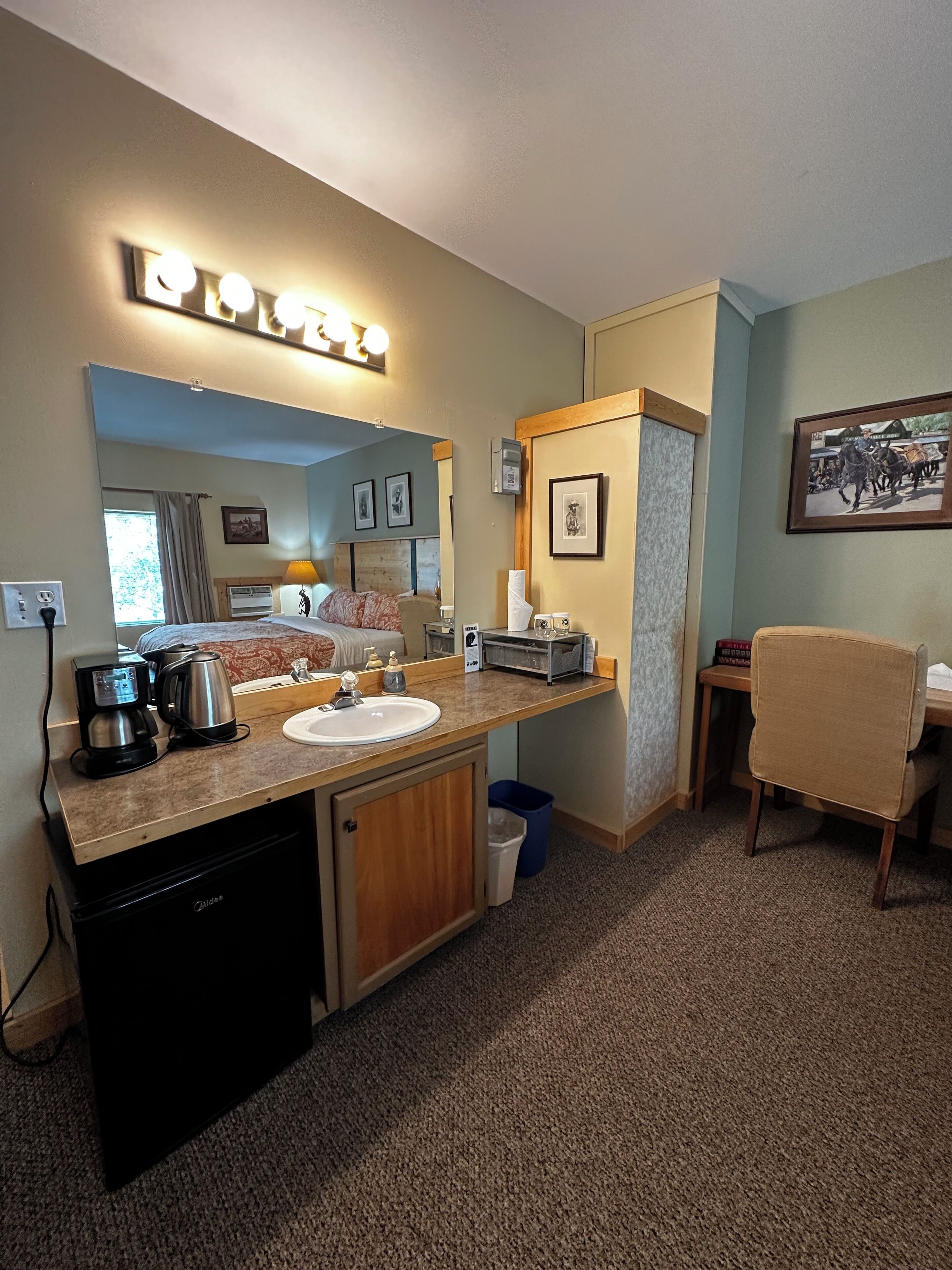 Habitación de hotel compacta con kitchenette, cama, pequeña zona de comedor y baño.