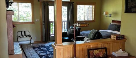 A cozy cabin interior with a wooden dining area, a kitchen with a bar, and a bedroom with a bed and books.