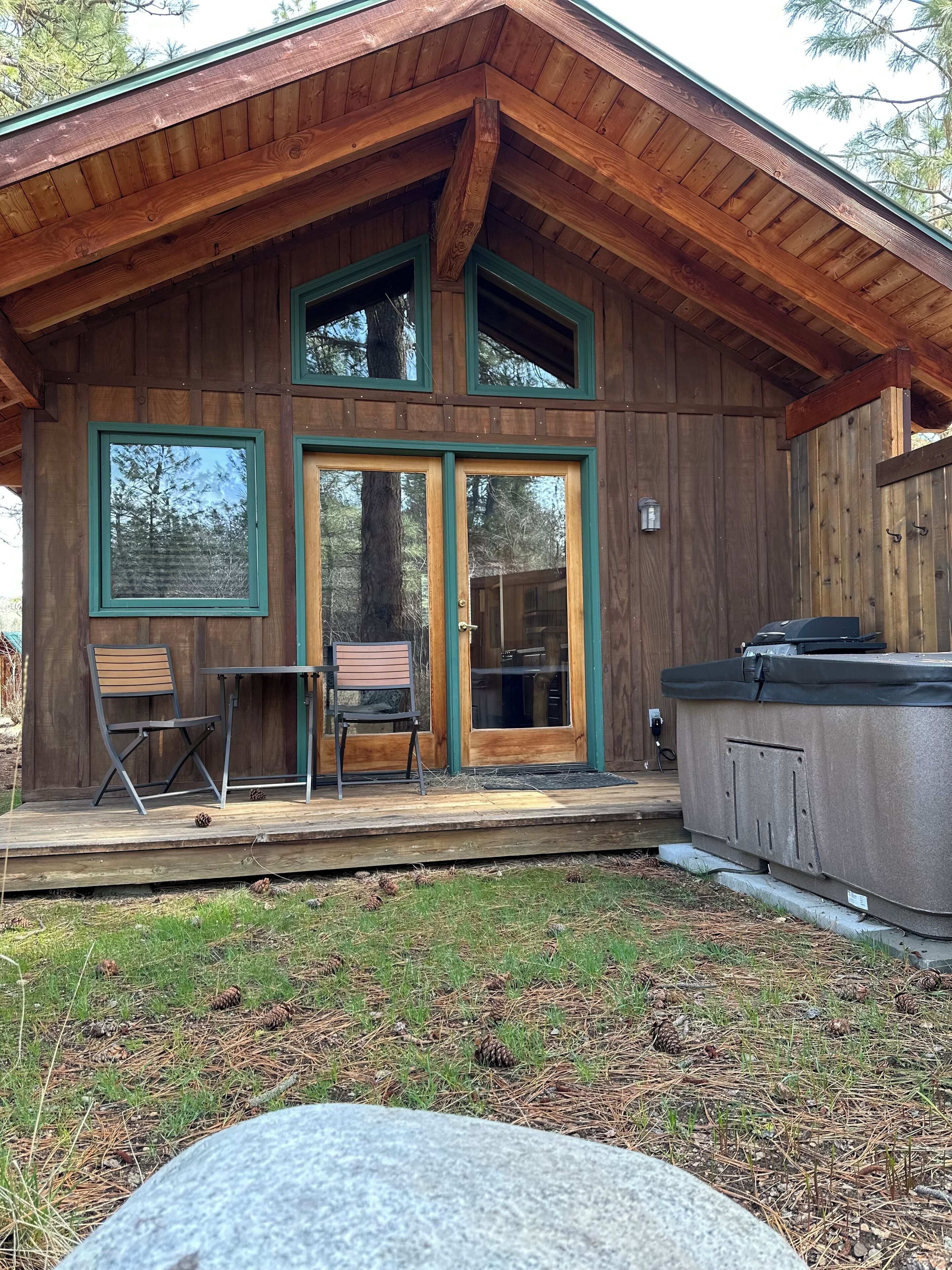 Une cabane en bois dotée d’une terrasse, de deux chaises et d’un bain à remous.