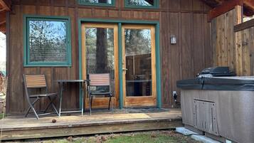 Une cabane en bois dotée d’une terrasse, de deux chaises et d’un bain à remous.