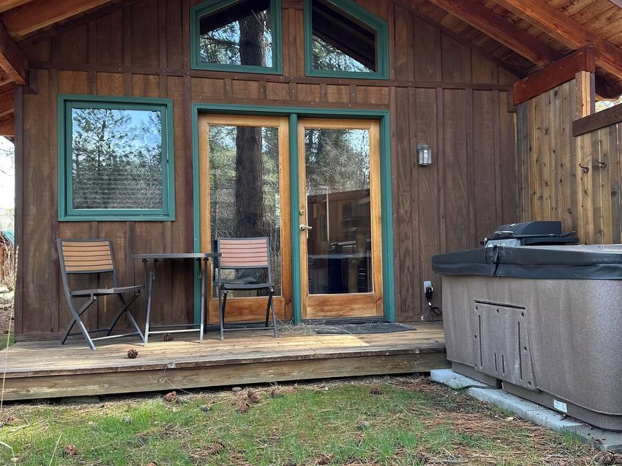 Une cabane en bois dotée d’une terrasse, de deux chaises et d’un bain à remous.