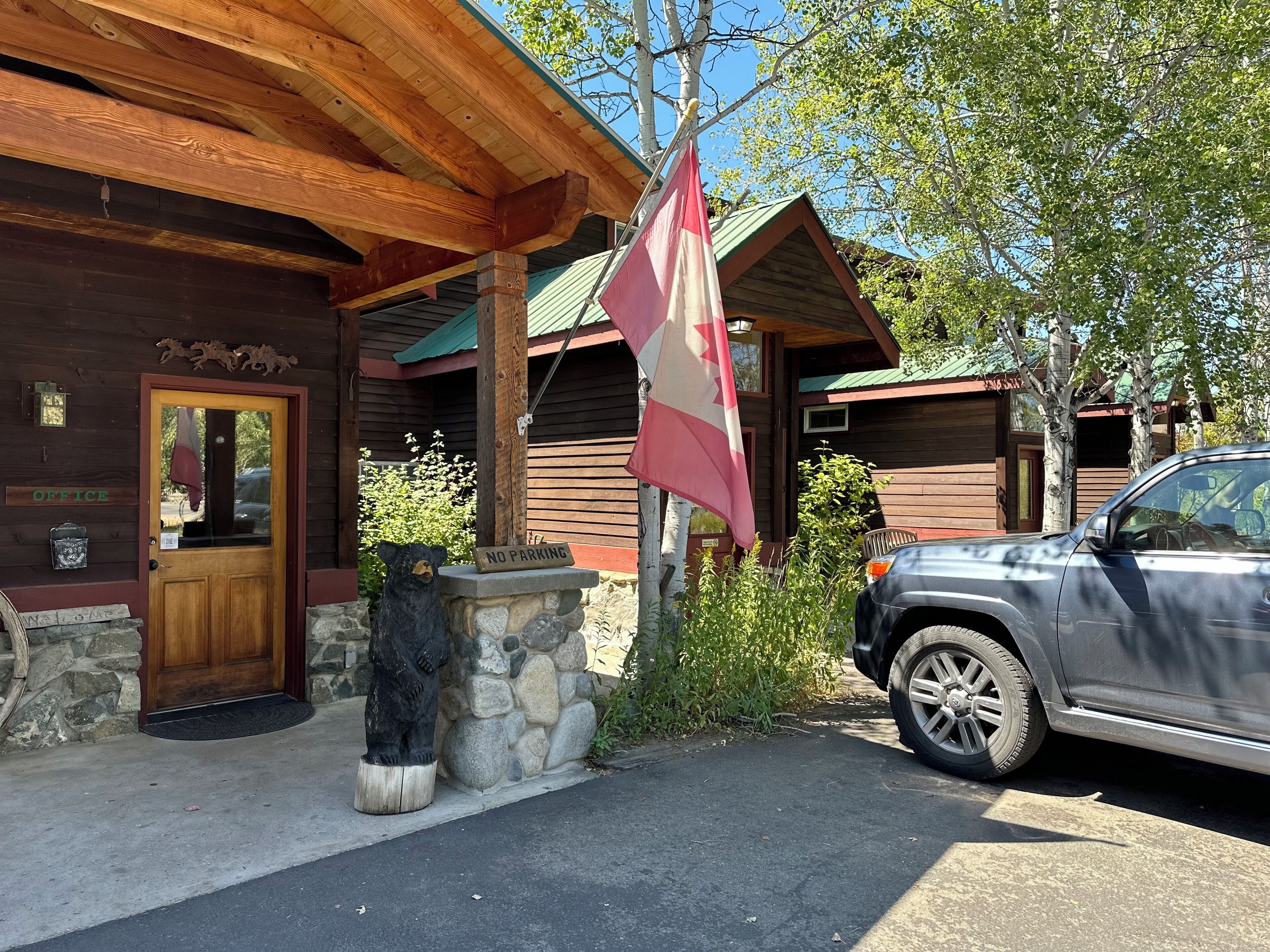 A lodge with a wooden exterior, a stone base, a bear statue, a 'NO PARKING' sign, and a flag.