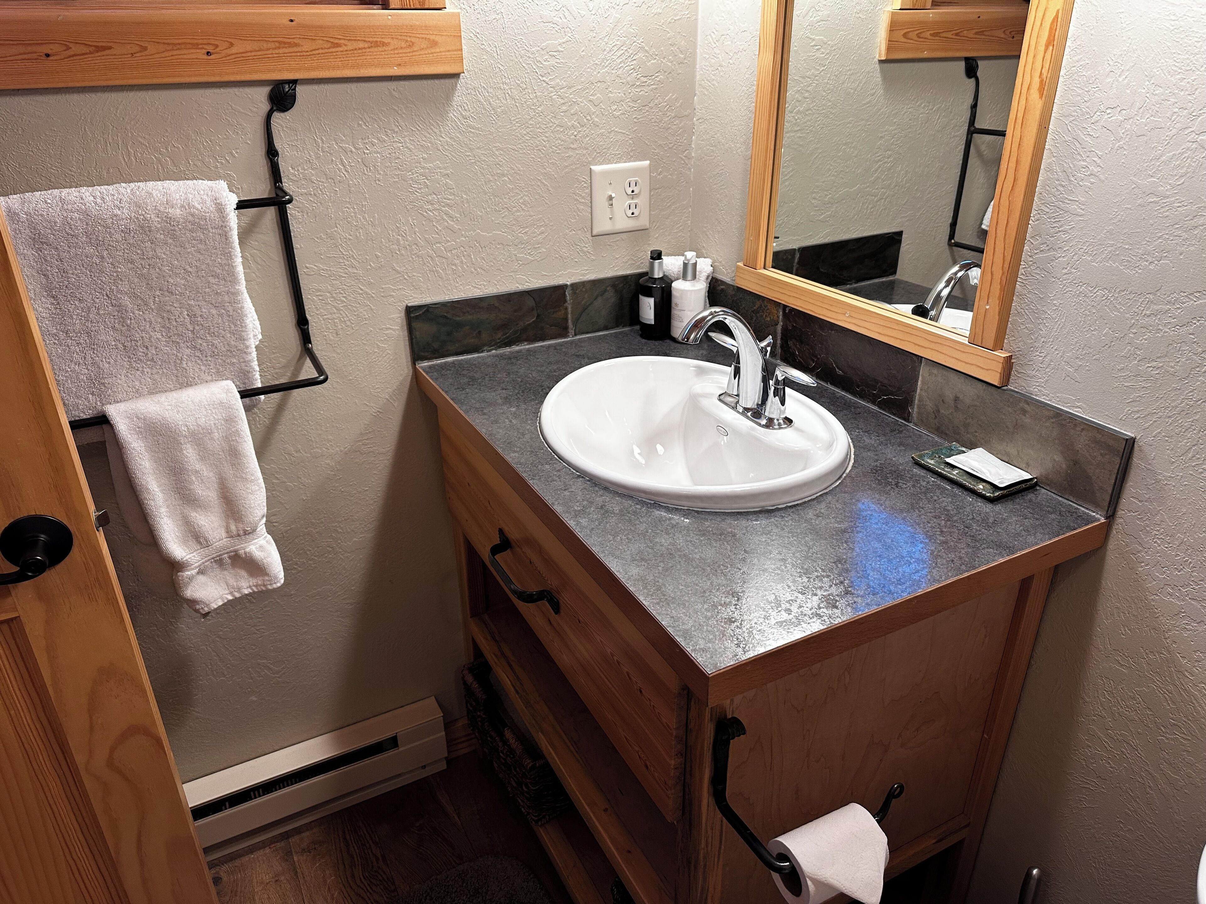 A bathroom with a white sink, wooden vanity, and a towel rack.