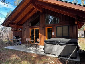 A wooden cabin with a patio, a grill, and a hot tub.