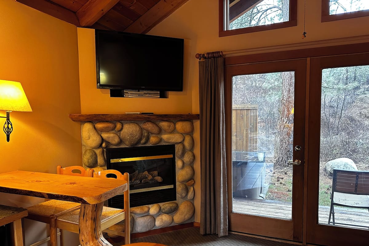 A cozy room with a stone fireplace, a television mounted above it, and a dining area with wooden furniture.