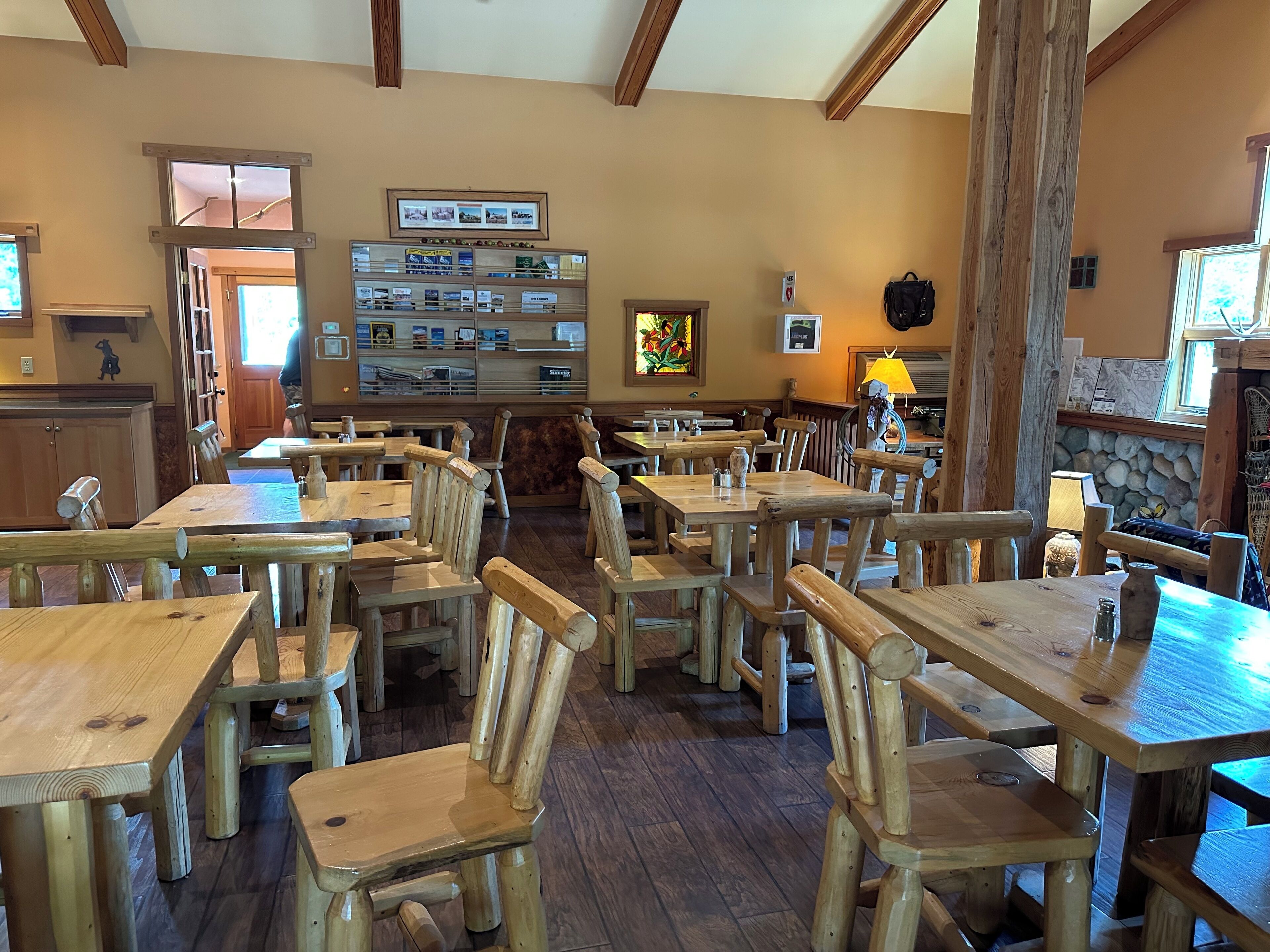 A rustic interior with wooden tables and chairs, a stone fireplace, and a display of local products.