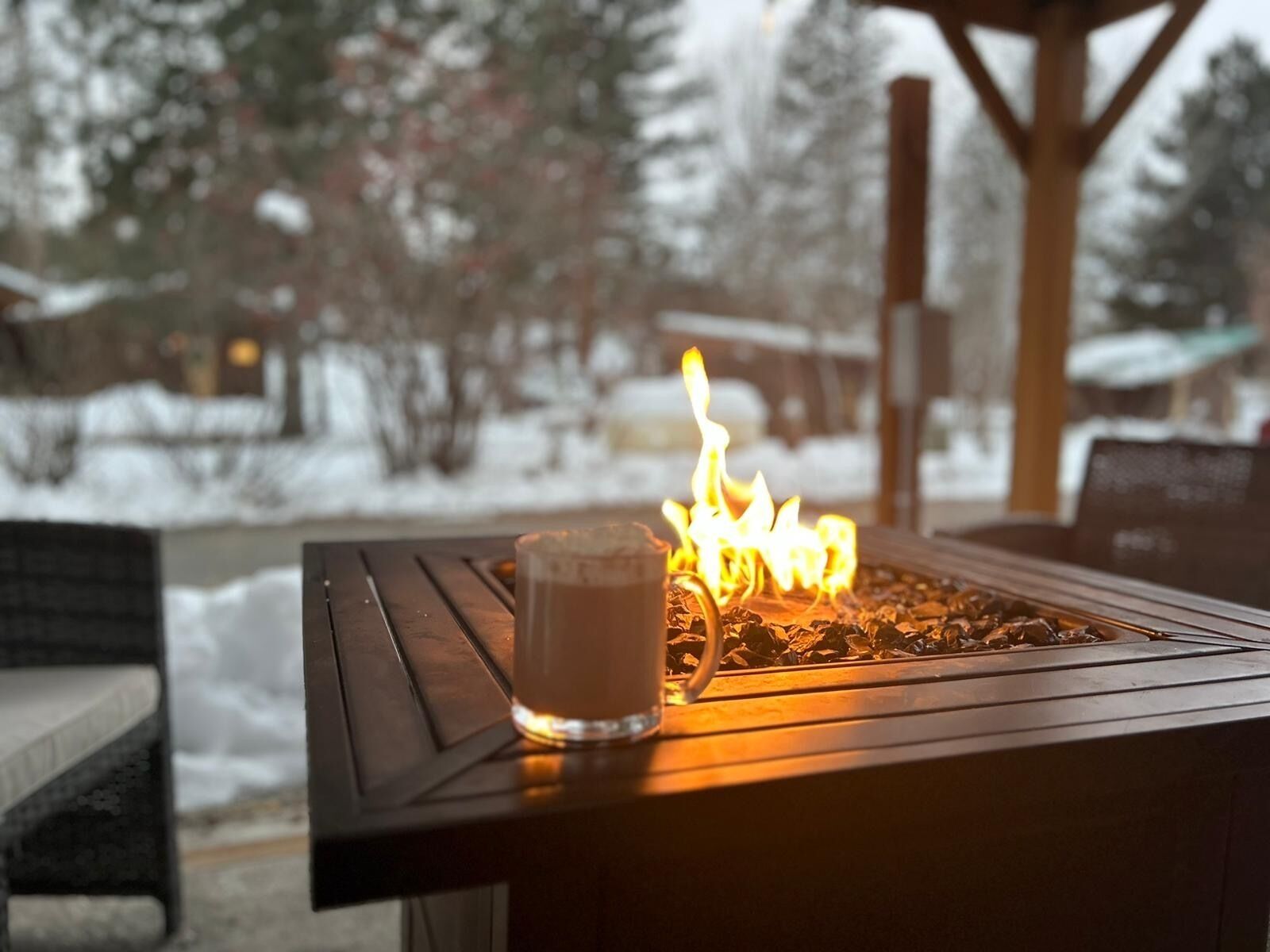 A wooden outdoor seating area with a fire feature and a glass of beverage.