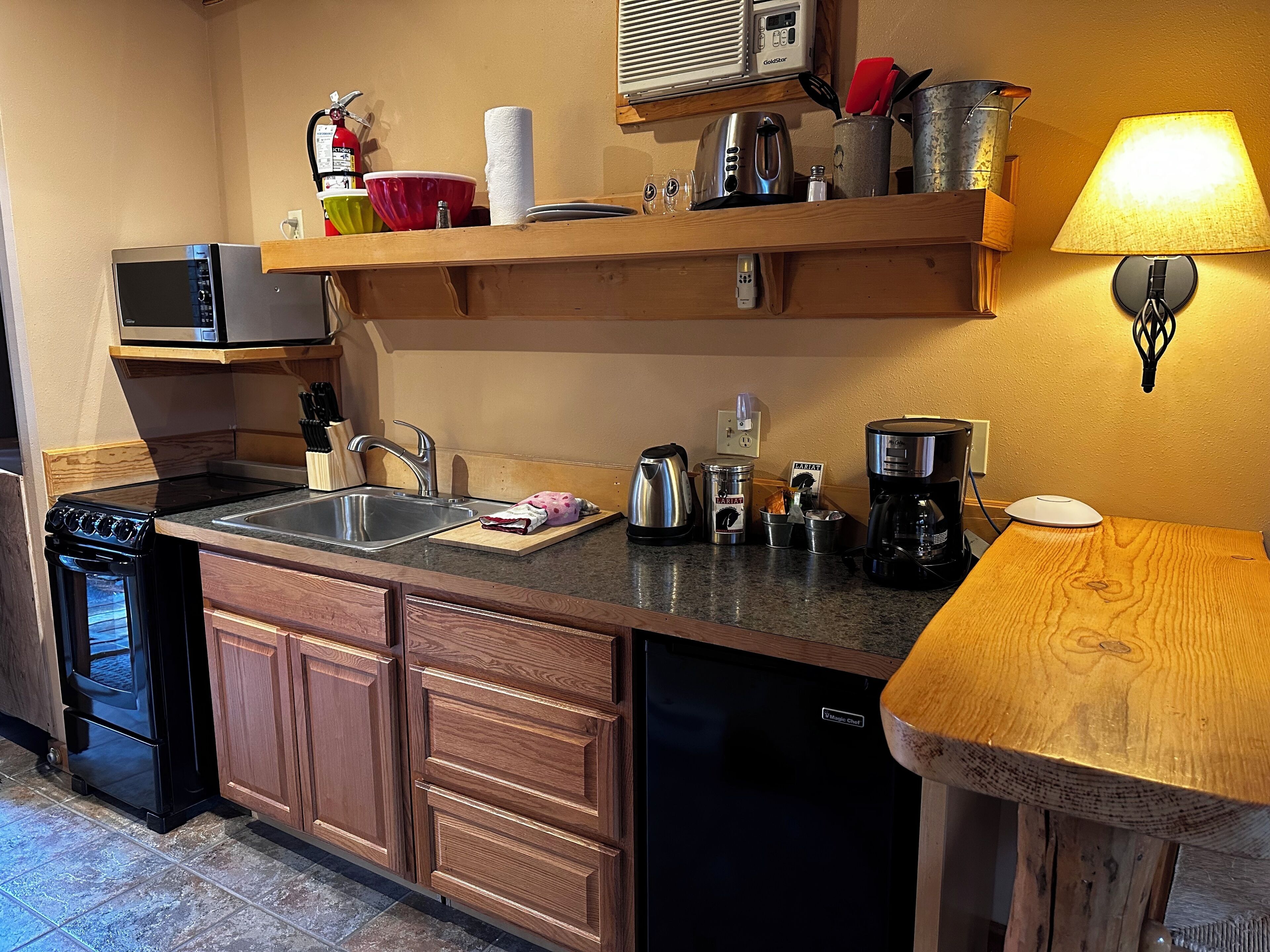 A compact kitchen with a stove, sink, microwave, and a coffee maker.