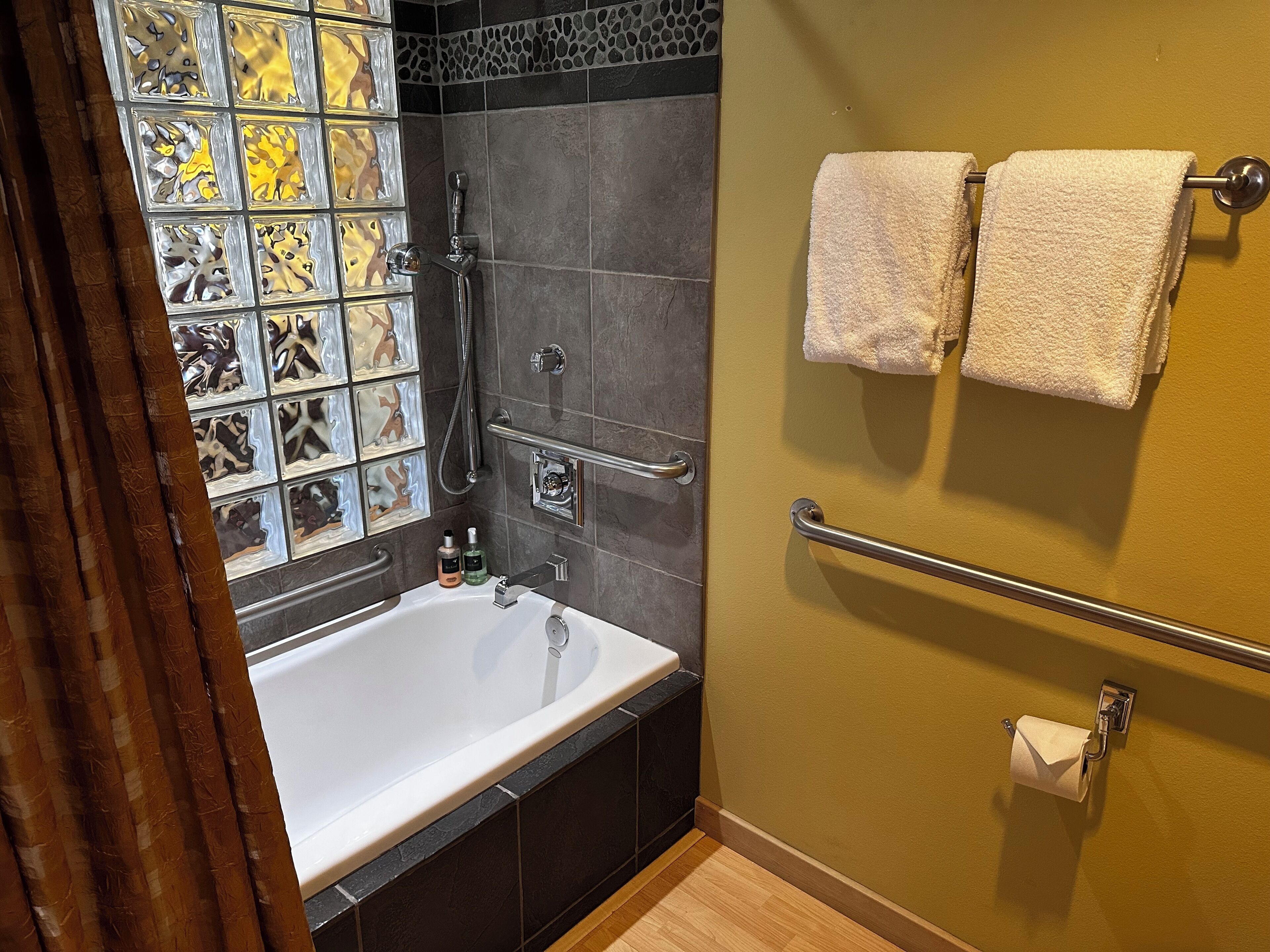 A bathroom with a bathtub, a shower, and a handrail.