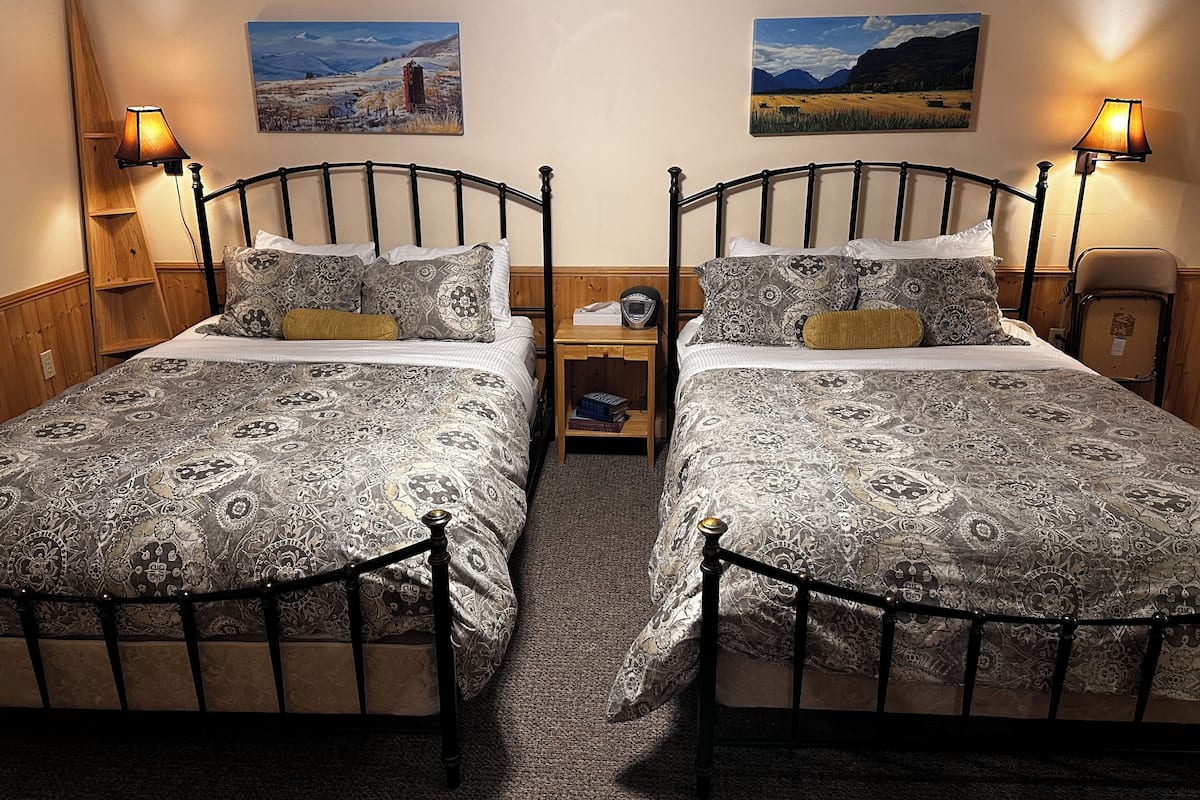 A double bed room with a wooden headboard, a nightstand, two bedside lamps, and two landscape paintings on the wall.