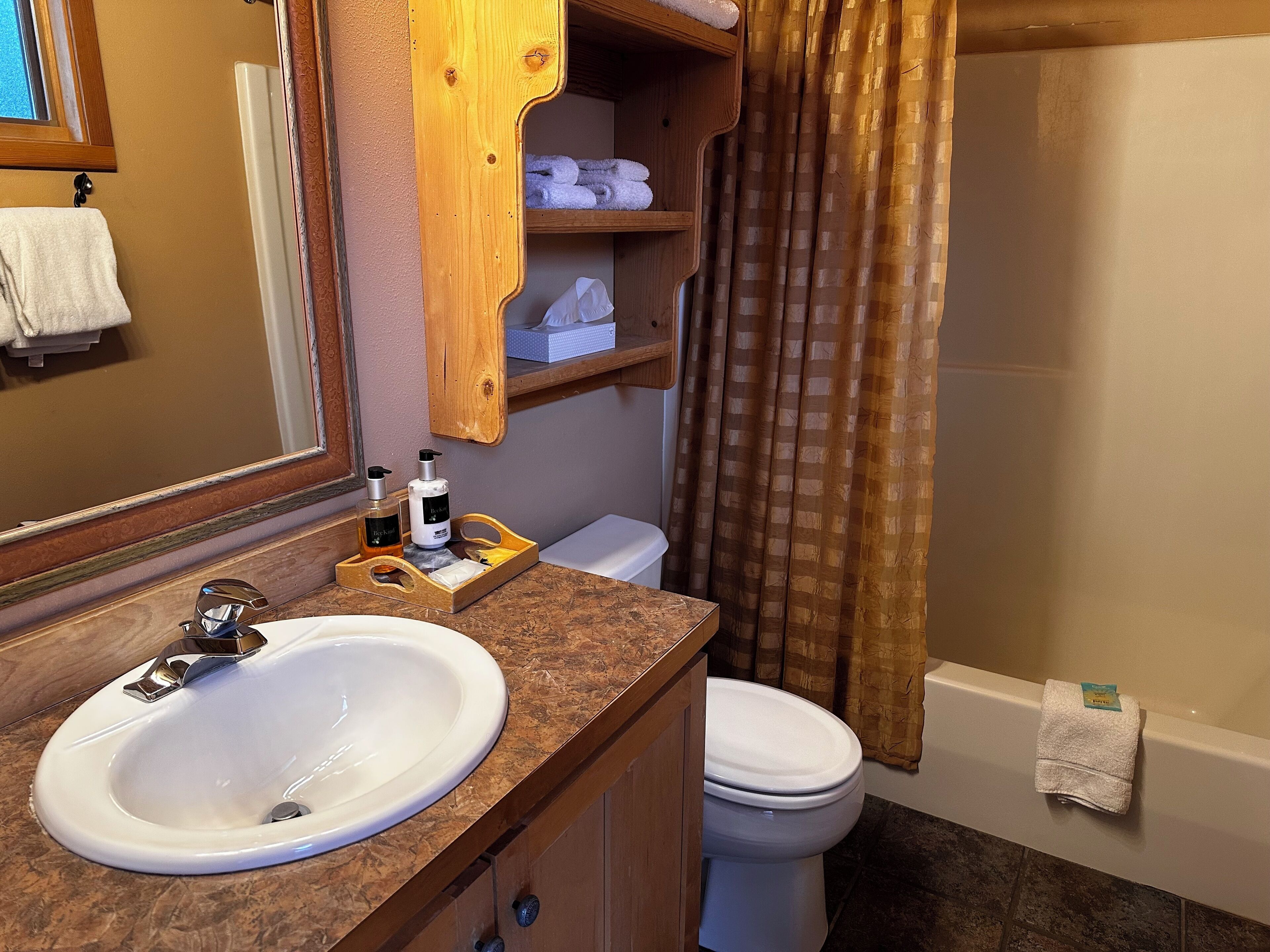 Une salle de bain avec un lavabo blanc, un meuble-lavabo en bois, des toilettes et un rideau de douche.