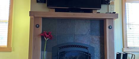 A fireplace with a television above it, a vase with a red flower, and a stone wall.