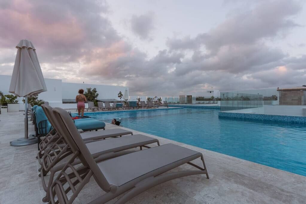 A rooftop pool area with lounge chairs and a person walking by.