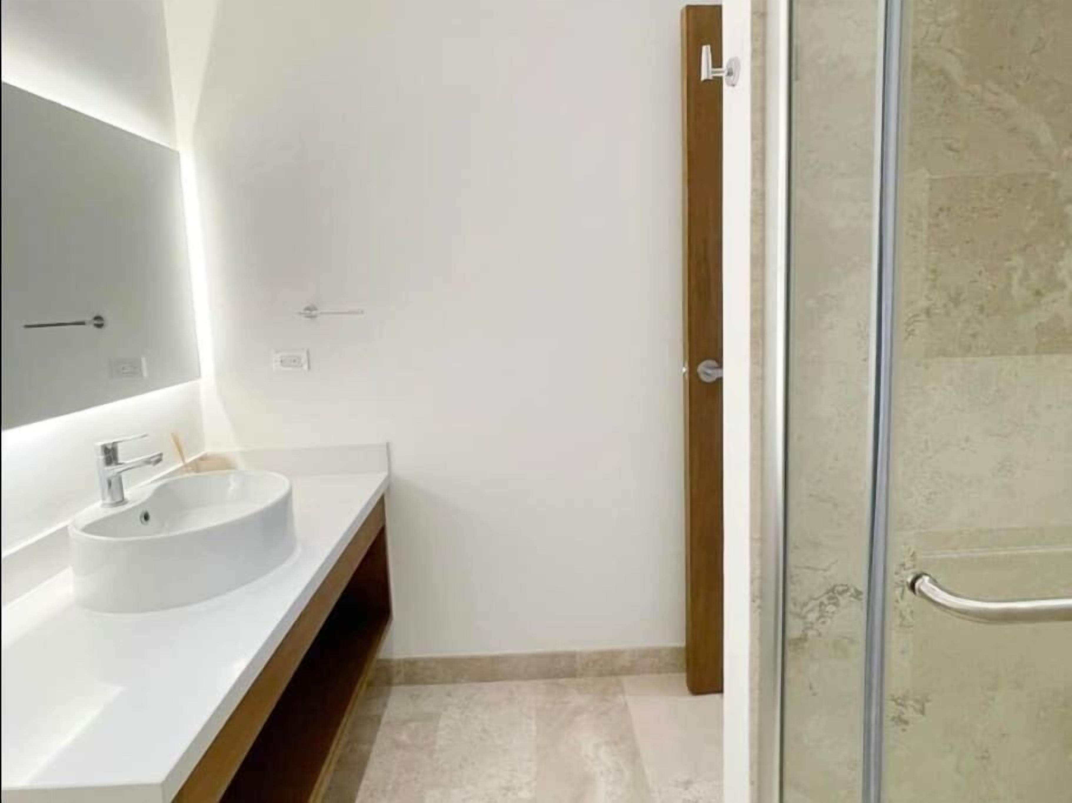 A modern bathroom with a white sink, a mirror, and a glass shower enclosure.