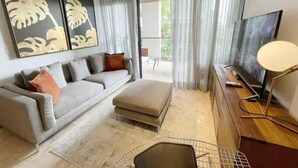 Un salon moderne avec un canapé gris, un petit pouf, un téléviseur posé sur un meuble en bois et un ventilateur de plafond.
