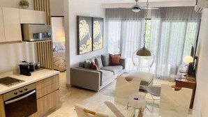 Une cuisine moderne dotée d’appareils électroménagers intégrés, un coin repas avec une table en verre et un salon avec un canapé et des rideaux.