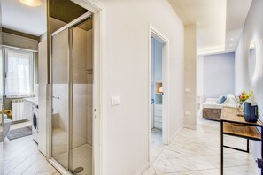 A modern hotel room with a shower, a bed, a bedside table, and a view of the hallway.